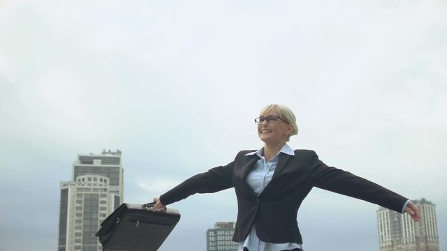 Inspired lady in formal suit holding bag and spinning outdoors, feeling happy