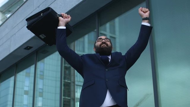 Extremely happy man in suit raising hands in winner gesture, profitable business