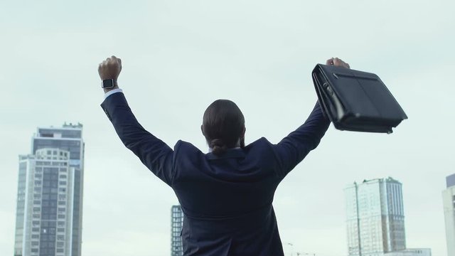 Handsome man in suit raising hands in winner gesture and turning to cam, success