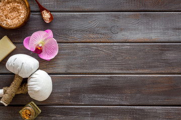 Massage table with thai herbal balls and orchids on dark wooden background top view frame copy space