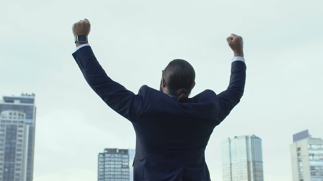 Cheerful male in business suit raising hands celebrating success, winner gesture