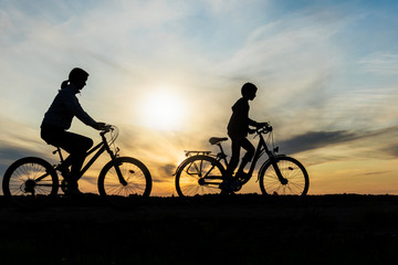 Boy and young girl riding bikes in countryside ,  silhouettes of riding persons at sunset in nature