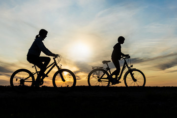 Fototapeta na wymiar Boy and young girl riding bikes in countryside , silhouettes of riding persons at sunset in nature