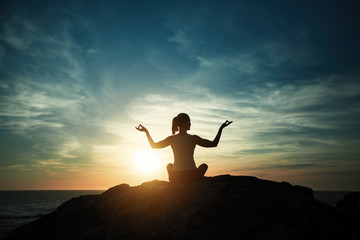 Silhouette of yoga woman sitting in Lotus position on the ocean beach during sunset.