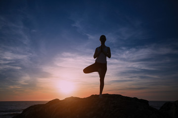Silhouette of woman standing at yoga pose on the ocean beach during sunset.