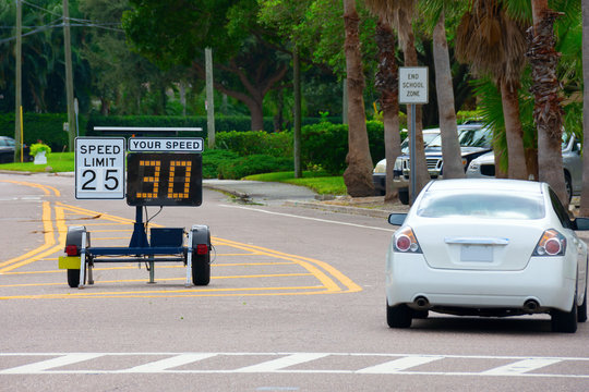 Radar speed limit indicator sign monitored by the police showing 30 miles per hour on the screen proving a passing car is speeding as it drives down the road in a clearly marked school zone.