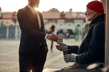 Homeless senior man hold out his hand to get money from unrecognizable rich man. Street life