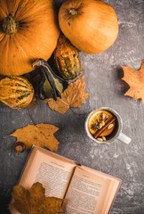 Relaxing moments with a hot beverage and book in the autumn arrangement full of pumpkins and maple leaves on the table.