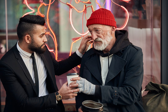 merciful businessman sit next to tramp in red hat and coat, rich man in black tuxedo