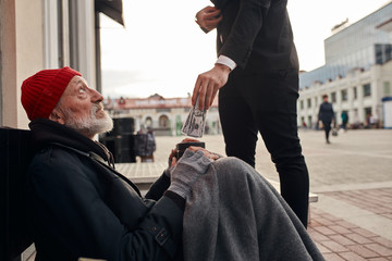 Male in suit gicing money to poor man sitting on street. Poverty, hunger