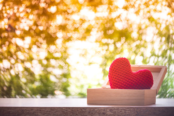 Red heart is made with yarn in the wooden box put on the table on bokeh background in the public park, for give support when people get who lack of desire with love and Valentine day concept.