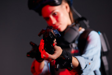 Young attractive female with VR shooter stand looking at camera, isolated over black background. Special device mask on head