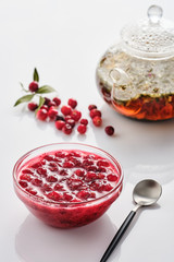 Cranberry jam in a glass bowl and teapot on a white background.