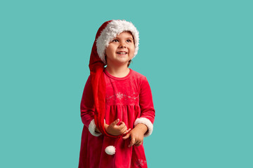 Adorable small baby girl in christmas hat and red dress on the studio background