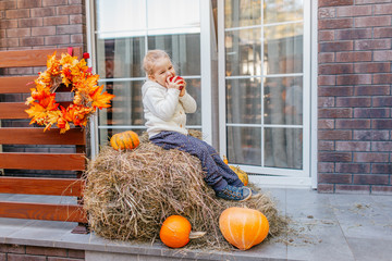 Adorable smiling Caucasian baby toddler in white knittes jacket sitting on the haystack with...
