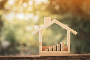 Stacking gold coins with growing interest value put in a wooden home model on bokeh background in the public park, Loan and business investment for real estate concept.