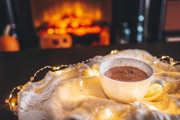 Cup of hot drink in front of warm fireplace. Holiday Christmas concept. White mug standing near fireside. Cozy relaxed magical atmosphere in a chalet.