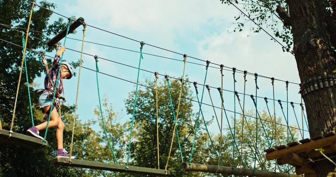Courageous preteen girl is on suspension bridge in rope park. Best holiday place in summer