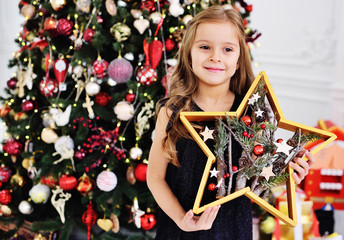 the child is a little cute girl in a smart black dress with a Christmas star in her hands on the...