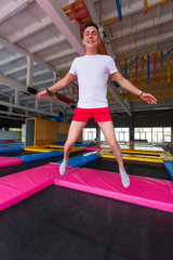 Fototapeta premium Fitness, fun, leisure and sport activity concept - Handsome happy man jumping on a trampoline indoors