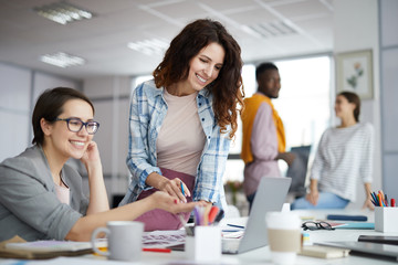 Portrait of two creative young women looking at laptop screen and smiling while discussing...