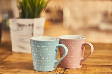 Two cups on wooden table, kitchen in the background.