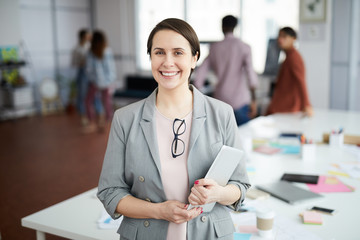Waist up portrait of smiling businesswoman looking at camera and holding digital tablet while...