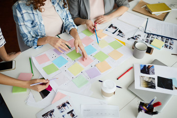 Above view of creative team planning startup project on table, focus on hands pointing at colorful sticky notes during meeting, copy space