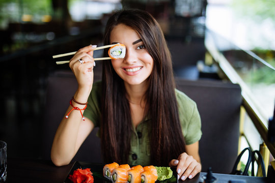 Young Woman Have A Sushi Holding Roll Under Her Eye In Cafe