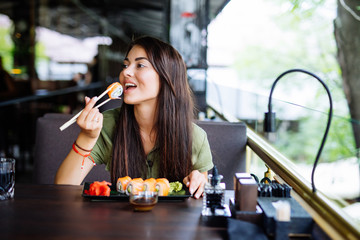 Beautiful young girl enjoying sushi in a cafe on a sunny day