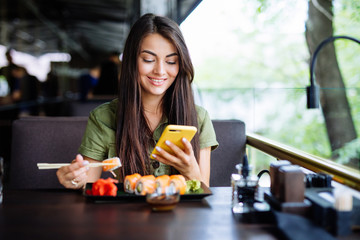 Young woman texting on the phone while eating sushi in a restaurant