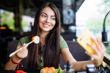 Young woman is taking a selfie photograph while eating sushi in cafe