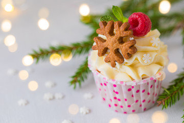 Christmas cupcakes or muffins with cream and raspberry, over the fir tree branches background