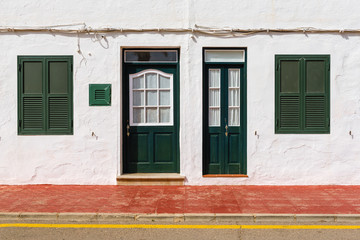 Traditional Spanish architecture with white facade and green doors and windows. Menorca, Spain