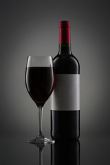 Bottle of red wine with label and wineglass on gradient background