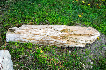 Fragment of a partially destroyed antique column of white marble with yellow veins. Antique artifact outdoors.