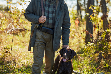 Cropped hunter man with gun and dog went hunting birds in forest