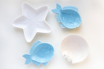 Empty plates in form of fish, starfish and shell in white and blue on light background. Minimal style pattern. Flat lay, top view