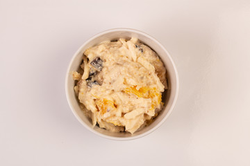 Salad of apple, orange, oat hops and prunes with honey in a white plate on a white background.