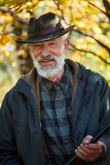 Naklejka na ściany i meble Mature bearded man holding gun, smiling, happy hunter looking at camera. Successful hunting