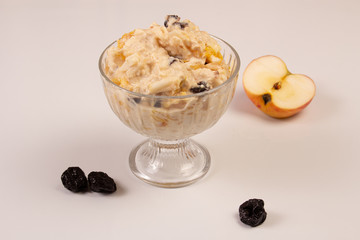 Salad of apple, orange, oat hops and prunes with honey in a glass plate on a white background. 