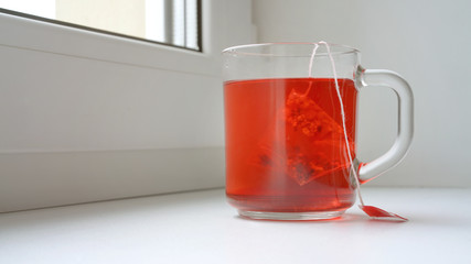 red fruit tea in glass cup with pyramid teabag on windowsill breakfast concept