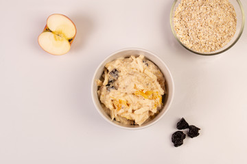 Salad of apple, orange, oat hops and prunes with honey in a white plate on a white background. 