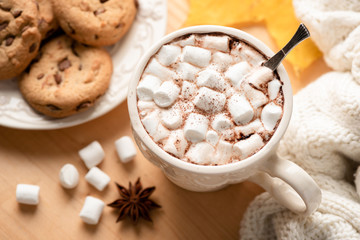 Hot chocolate mug with marshmallows and chocolate chip cookies on wooden table, top view