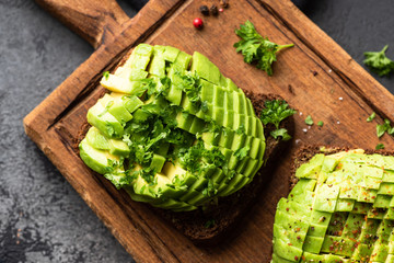 Rye bread toast with avocado and cilantro on a wooden cutting board. Closeup view. Healthy green food
