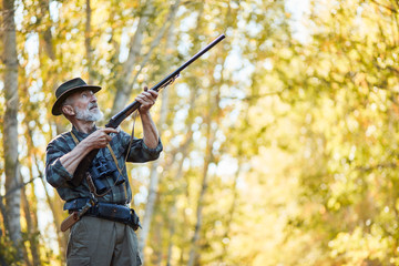 Hunting on wild birds in forest. Caucasian senior man hunt on birds, using gun. Hunter wearing...