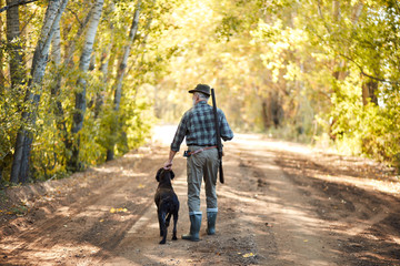 Senior hunter holding dog after hunting on ducks. Rear view on hunter