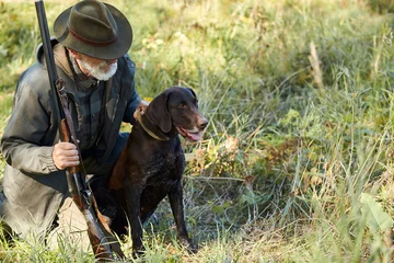 Zelfklevend Fotobehang Senior hunter and his dog in forest, look for prey, hunting on wild animals. Hunting season © alfa27