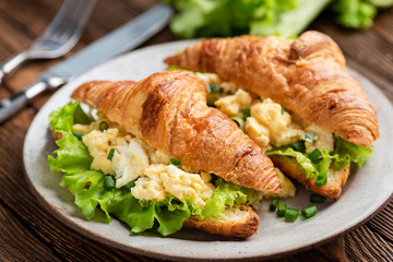 Breakfast croissant sandwich with scrambled eggs and green lettuce salad
