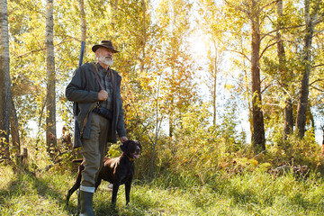 Senior hunter and his dog in forest, look for prey, hunting on wild animals. Hunting season